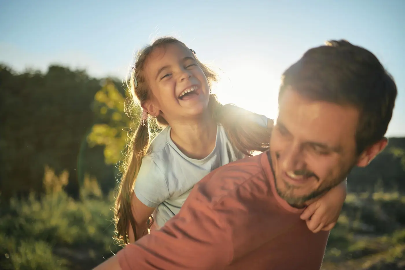 A laughing child on her father's back in warm evening sunlight