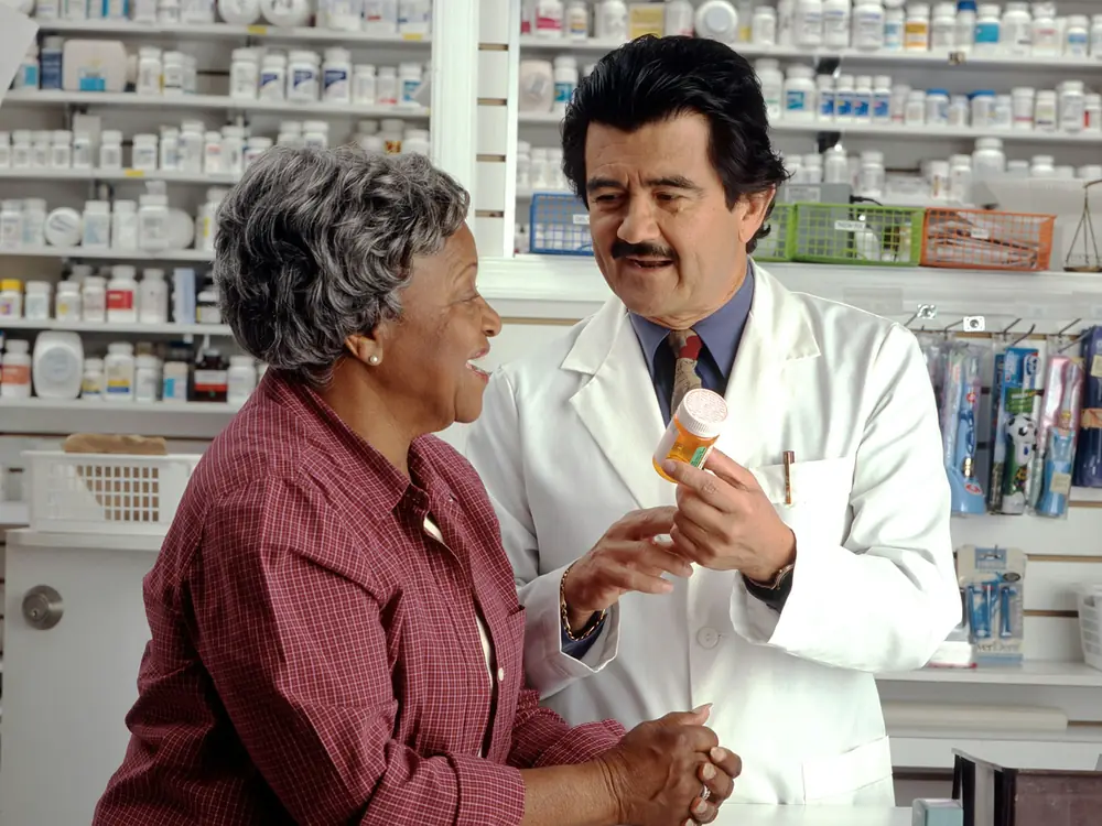 A pharmacist shows a prescription bottle to a smiling customer